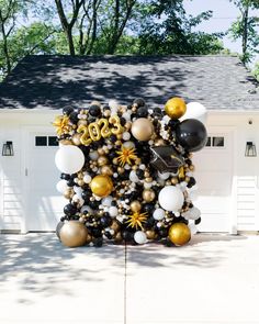 a large balloon arch is decorated with black, gold and white balloons in front of a garage