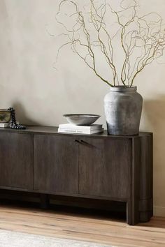 a vase with some branches in it sitting on top of a wooden table next to a wall