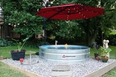 an outdoor hot tub in the middle of a yard with a red umbrella over it