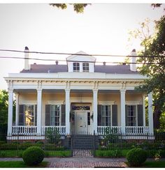 a white house with columns and pillars on the front porch is surrounded by greenery