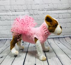 a small dog wearing a pink sweater on top of a white wooden floor next to a brick wall