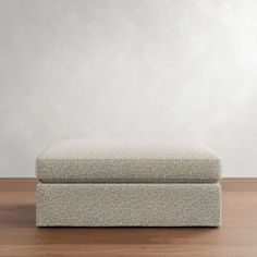 an upholstered footstool sitting on top of a hard wood floor in front of a white wall