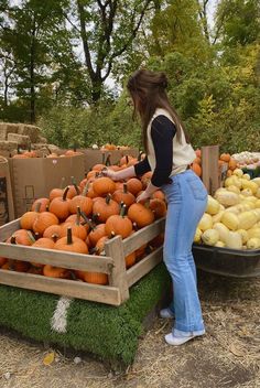 a woman standing next to a pile of pumpkins on display in a field with boxes full of them