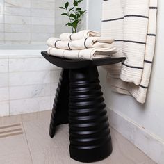 a black stool sitting in front of a bath tub next to a towel rack with towels on it