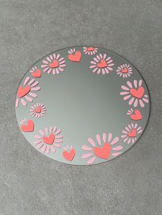 a round mirror with hearts and flowers painted on the side in pink, grey and white