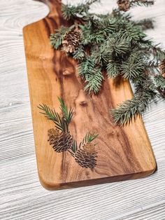 a wooden cutting board with pine cones and evergreen needles on it, sitting on a table