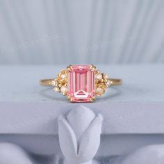 a pink tourmaline and diamond ring sitting on top of a white cloth covered box