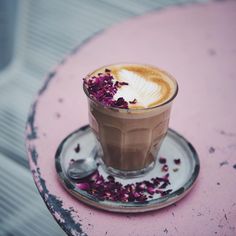 a cappuccino with purple sprinkles is on a saucer