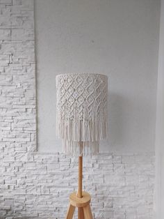 a white table lamp with a wooden base and fringe shade on it in front of a brick wall