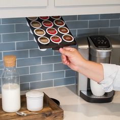 a person is holding up a box of milk in front of a coffee maker with several stickers on it