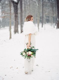 the bride is walking through the snow in her wedding dress and fur stole with flowers