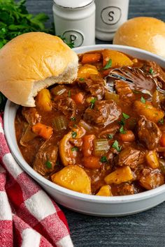 a bowl filled with beef stew next to two rolls