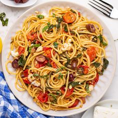 a plate of pasta with tomatoes, spinach and fettuccine on a marble table