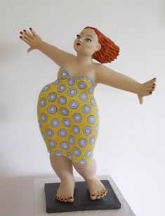 a statue of a woman in a yellow dress with her arms spread out and hands outstretched