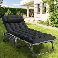 a black chaise lounge chair sitting on top of a lush green field next to a house