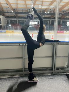 a woman standing on one leg in front of an ice rink