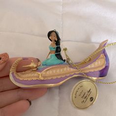 a hand holding a small figurine of a woman on a purple and gold boat