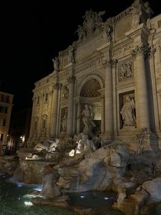 an ornate building lit up at night with water running down the side and statues on top