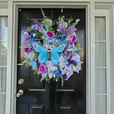 a blue and purple butterfly wreath on the front door of a house with black doors