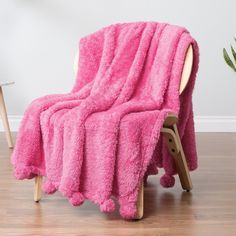 a pink blanket sitting on top of a wooden chair next to a potted plant