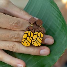 a woman's hand holding a pair of earrings with yellow and brown designs on them