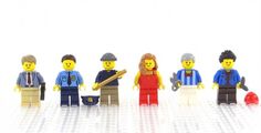 a group of lego people standing next to each other on a white surface with one person holding a baseball bat