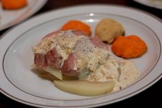 a white plate topped with meat covered in gravy next to potatoes and carrots