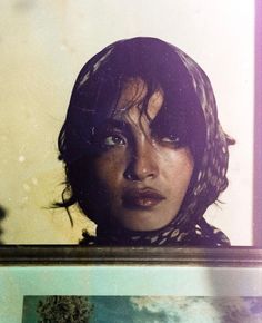 a woman is looking at the camera through a glass window with her hair blowing in the wind