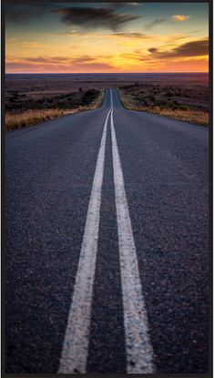 an empty road with two white lines painted on it at sunset in the middle of nowhere