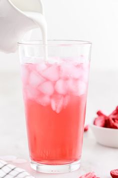 a pitcher pouring ice into a glass filled with pink liquid and raspberries on the side