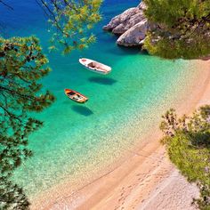 two boats floating on top of a blue body of water next to a sandy beach