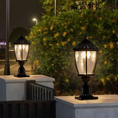 two lamps are lit up on the side of a building in front of some bushes