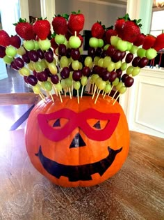 a pumpkin shaped vase filled with grapes and strawberries on top of a wooden table