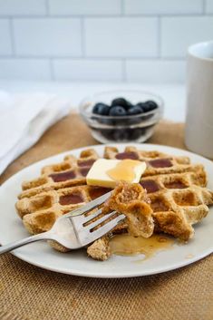 a white plate topped with waffles covered in butter and blueberries next to a cup of coffee