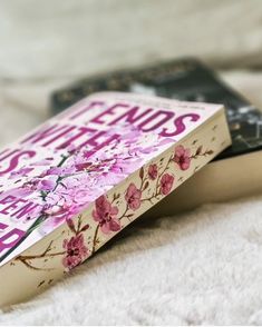 a book sitting on top of a bed next to a white blanket and pillow with pink flowers