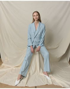 a woman sitting on top of a white sheet wearing a blue suit and white shoes