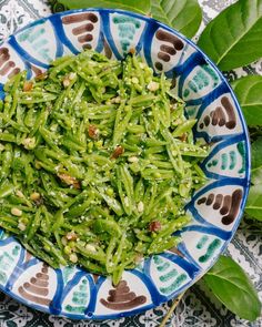 a blue and white bowl filled with green food on top of a patterned table cloth