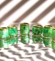 several green glass candles sitting on top of a reflective surface with the light reflecting off them