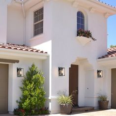 a white house with two garages and plants in the front yard on a sunny day