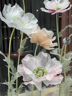 some white and pink flowers in front of a black fence with green stems on it