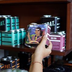 a person holding up a can in front of some cans on a shelf with other items