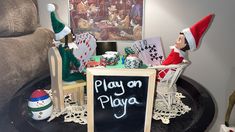 an elf is sitting in a chair next to a sign that says play on playa