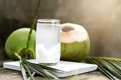 a glass of water sitting on top of a wooden table next to an open coconut