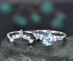 two rings with blue topazte and white diamonds on a rock in front of a blurry background