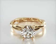 a yellow gold engagement ring with a round cut diamond in the center, on a white background