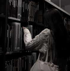 a woman picking up a book from a bookshelf