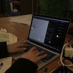 a person using a laptop computer on a wooden table with books and papers around them