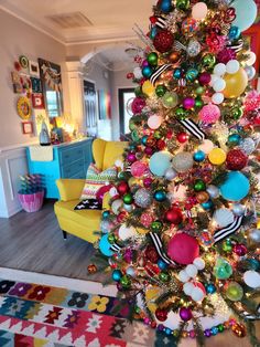 a brightly colored christmas tree in a living room decorated with ornaments and balloons on it