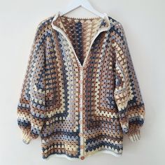 a crocheted sweater hanging on a hanger next to a white wall with an open hood