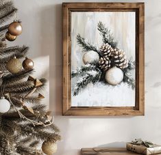 a painting hanging on the wall next to a christmas tree with balls and pine cones